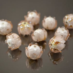 May include: Ten pink glass beads with a white center and gold accents. The beads are shaped like flowers with multiple petals.