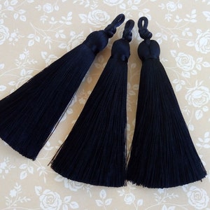 May include: Three black tassel trim embellishments. Each tassel is made of a long, thin, black thread and has a small, round, black knot at the top.