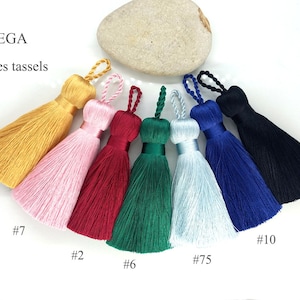 Peut inclure: Huit pompons de différentes couleurs, chacun mesurant 10 cm de long. Les pompons sont disposés en cercle sur un fond blanc. Les couleurs sont : or, rose, rouge, vert, bleu clair, bleu foncé et noir.
