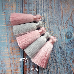 May include: Five tassels in pink and light gray with gold metal rings. The tassels are arranged in a fan shape. The text #75 and #79 is visible at the bottom of the image.