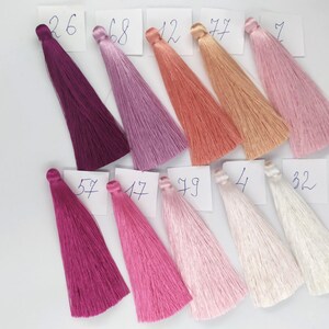May include: A collection of 10 silk tassels in various shades of pink, purple, and white. The tassels are labeled with numbers from 4 to 79.