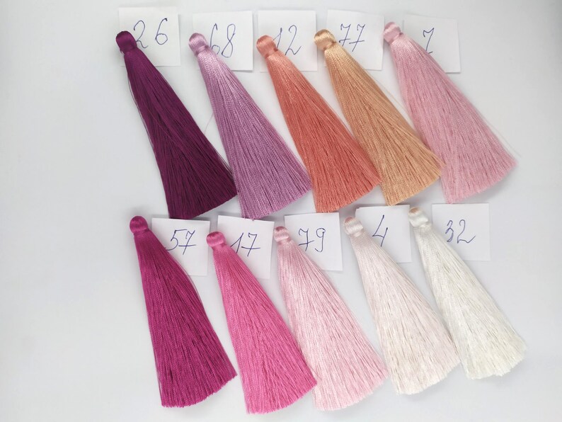 May include: A collection of 10 silk tassels in various shades of pink, purple, and white. The tassels are labeled with numbers from 4 to 79.