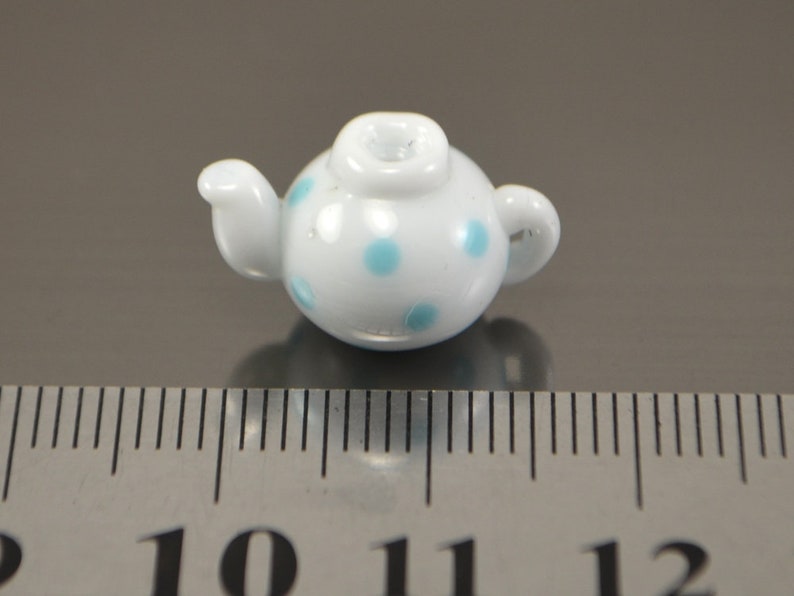 Puede incluir: Una tetera blanca peque&ntilde;a con lunares azules. La tetera mide aproximadamente 2,5 cm de alto y est&aacute; hecha de cer&aacute;mica.