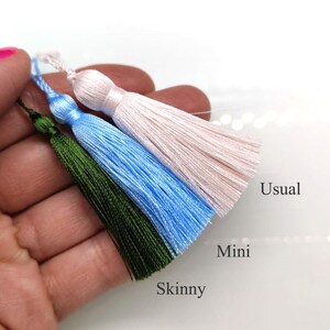 May include: Three colorful tassels in shades of green, blue, and pink are displayed. The tassels are labeled "Usual", "Mini", and "Skinny". The tassels are held in a hand against a white background.
