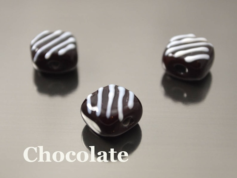 May include: Three chocolate candies with white stripes on top. The candies are arranged in a triangular pattern on a silver surface.