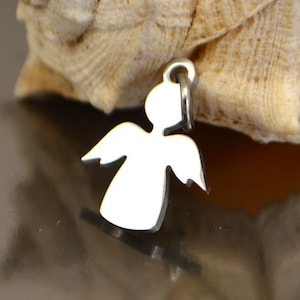 Puede incluir: Un colgante de ángel de plata con un acabado liso y pulido. El encanto tiene la forma de un ángel simple con las alas extendidas.