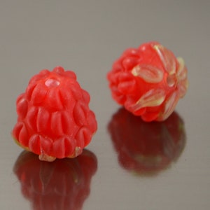 May include: Two red glass beads shaped like raspberries. The beads have a textured surface and a small hole in the center.