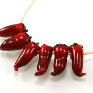 May include: A necklace featuring red glass chili pepper beads strung on a beige cord.