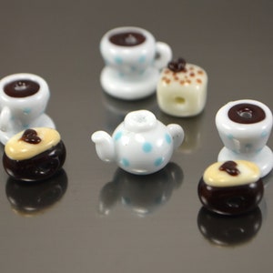Puede incluir: Un juego de tazas de t&eacute; y tetera en miniatura con lunares azules y un interior marr&oacute;n. Tambi&eacute;n hay dos pasteles en miniatura con glaseado marr&oacute;n y blanco.