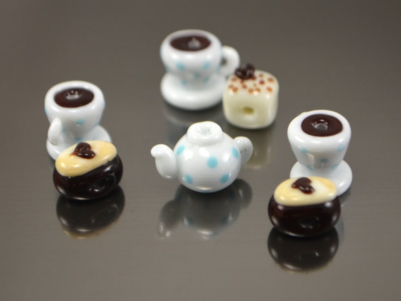 Puede incluir: Un juego de tazas de t&eacute; y tetera en miniatura con lunares azules y un interior marr&oacute;n. Tambi&eacute;n hay dos pasteles en miniatura con glaseado marr&oacute;n y blanco.