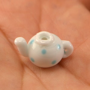 Puede incluir: Una tetera blanca peque&ntilde;a con lunares azules. La tetera tiene un pico y una asa.