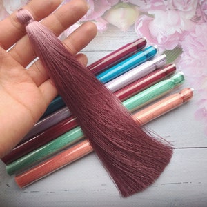 Peut inclure: Un ensemble de huit pompons en soie colorés dans différentes nuances de rose, bleu, vert et orange. Les pompons sont emballés dans des tubes en plastique transparents.
