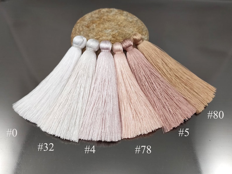 May include: Six different shades of white and pink tassels, from white to light pink to brown. The tassels are arranged in a row from left to right, with the lightest shade on the left and the darkest shade on the right. The tassels are labeled with numbers: #0, #32, #4, #78, #5, and #80.