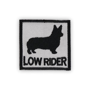 May include: Square patch with a black silhouette of a corgi dog on a white background, framed by a black border. The words "LOW RIDER" are embroidered in white below the dog.