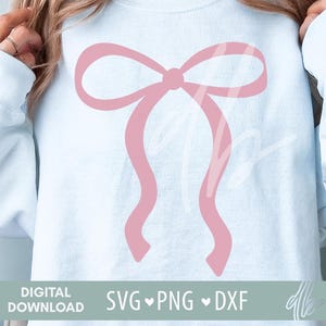 Könnte beinhalten: Ein hellblaues Sweatshirt mit einem rosafarbenen Schleifendesign. Das Design ist eine einfache, stilisierte Schleife mit abgerundeten Kanten.