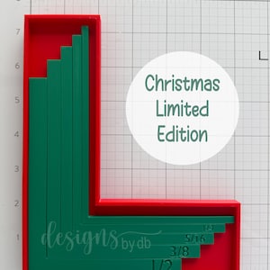May include: A red L-shaped frame containing nested green L-shaped guides with measurements 1/2, 3/8, 5/16, and 1/4 printed on them. A white circle features the text Christmas Limited Edition. The object is positioned on a grid with inch markings.