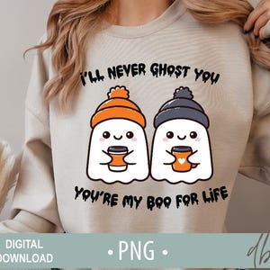 May include: A light grey sweatshirt with a graphic of two ghosts holding coffee mugs. The text "I'll never ghost you, you're my boo for life" is printed on the sweatshirt.
