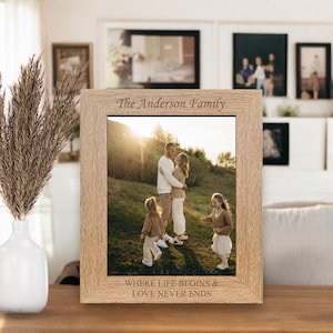 May include: A wooden photo frame with a light brown finish. The frame features a photo of a family of four in a field. The text "The Anderson Family" is engraved at the top of the frame. The text "Where life begins & love never ends" is engraved at the bottom of the frame.