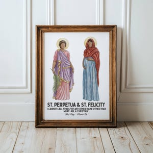 May include: Framed artwork featuring watercolor illustrations of St. Perpetua and St. Felicity. St. Perpetua is depicted in pink and purple robes, holding a palm branch. St. Felicity is in a blue dress and red shawl. Text reads "I CANNOT CALL MYSELF BY ANY OTHER NAME OTHER THAN WHAT I AM, A CHRISTIAN."