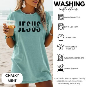 A woman wearing a teal green T-shirt with the text "JESUS Christ is King" printed on it, holding a drink. The image also includes instructions for washing the T-shirt, including machine washing cold, dry in low heat, hanging dry, turning the garment inside out, avoiding fabric softeners, and not bleaching.