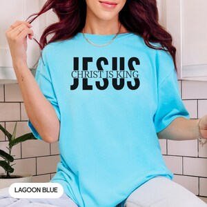 A woman wearing a blue t-shirt with the text "JESUS IS KING" printed on it.