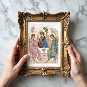 May include: A framed watercolor painting depicting three figures in robes, with halos, seated around a table. The painting is in a gold ornate frame. The figures are in shades of pink, blue, and green. The background has a light brown and beige color.