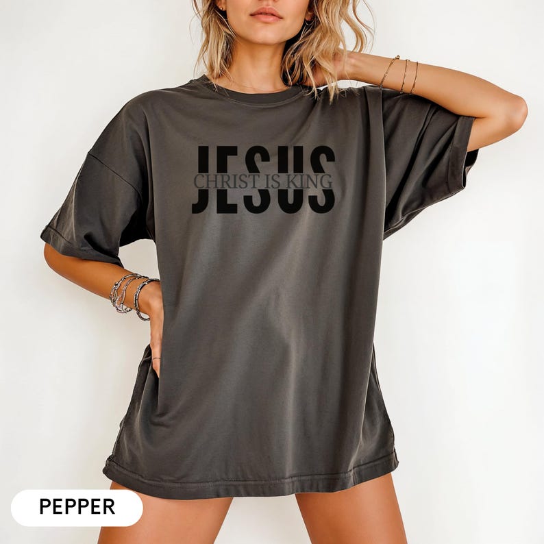A woman wearing a gray t-shirt with the text "JESUS CHRIST IS KING" printed on it.