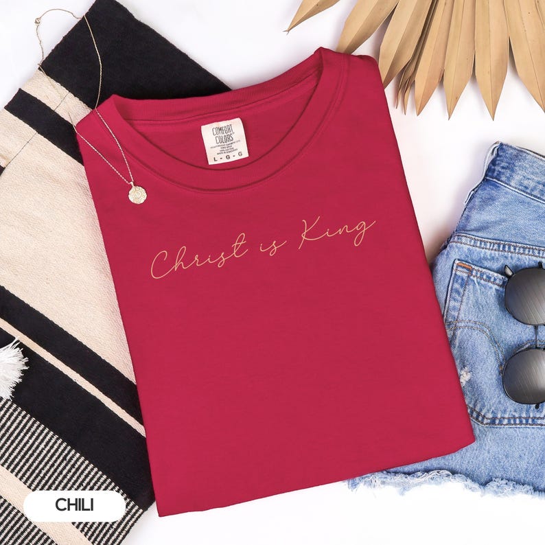 a red t-shirt with the text "Christ is King" printed on it, along with a pair of denim shorts and sunglasses.