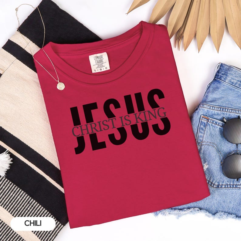 a red t-shirt with the text "JESUS IS KING" printed on it, along with a pair of denim shorts and sunglasses.