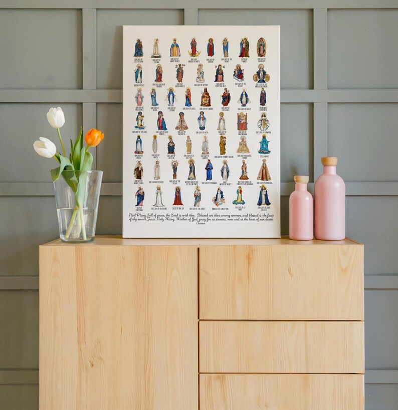 May include: A framed print featuring numerous religious figures in various poses and attire. The print is displayed on a light wooden cabinet, accompanied by two pink bottles and a vase of tulips. The text at the bottom of the print is partially visible.