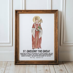 Könnte beinhalten: Ein gerahmter Druck mit einer Aquarellillustration von St. Gregor dem Großen. Er ist in einem roten Gewand dargestellt, das einen Stab und ein Buch hält, mit einem goldenen Heiligenschein. Der Druck enthält Text über seine Lehren und den Festtag.