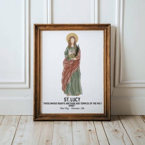 May include: Framed watercolor print of St. Lucy, depicted in a green dress and red shawl, holding a book and palm frond. The print includes the text "ST. LUCY" and a quote, with "Feast Day December 13th" at the bottom. The frame is a warm brown.