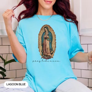 May include: Lagoon blue t-shirt with an image of the Virgin Mary in a gold oval frame. The words "pray like a mom" are written in a script font below the image. The shirt is a solid colour.