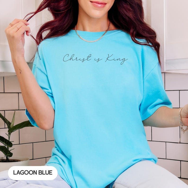 A woman with long, dark hair wearing a light blue t-shirt with the text "Christ is King" printed on it.