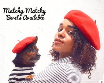 May include: A person wearing a red beret holds a small dog wearing a red beret and a black and white striped shirt. The text "Matchy-Matchy Berets Available" is at the top of the image. The text "IG @aleighawstorm IG @theoriginalhairhythm" is at the bottom of the image.