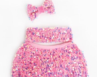 May include: Pink sequin newborn outfit with a matching pink velvet bow headband. The outfit is made of soft, stretchy fabric and is perfect for newborn photoshoots.