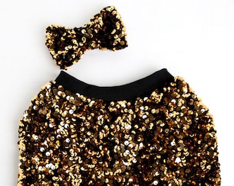 May include: Gold sequin skirt with a black waistband and a matching gold sequin bow.