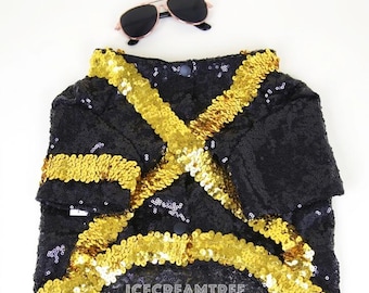 May include: A black sequined garment featuring gold sequin trim arranged in a crisscross pattern across the front, accompanied by a pair of black sunglasses with gold frames. The text ICECREAMTREE STUDIO is printed in white at the bottom.