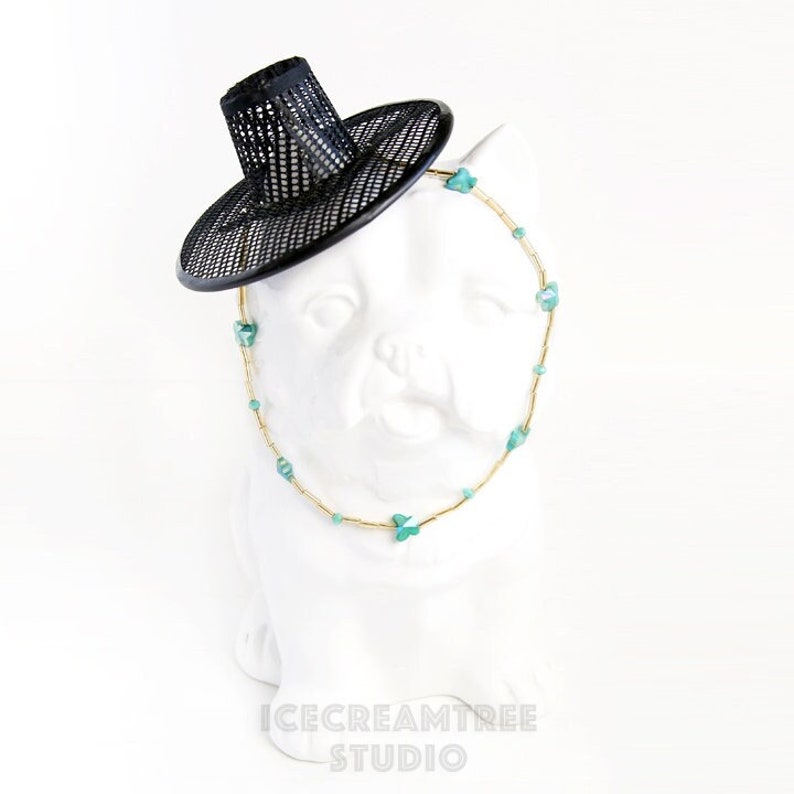 May include: A white ceramic bust of a cat wearing a black mesh hat and a gold chain necklace with turquoise butterfly charms.