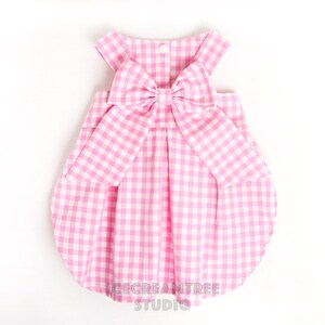 Puede incluir: Vestido de beb&eacute; de vichy rosa y blanco con un gran lazo en la espalda. El vestido tiene una falda fruncida y es sin mangas.