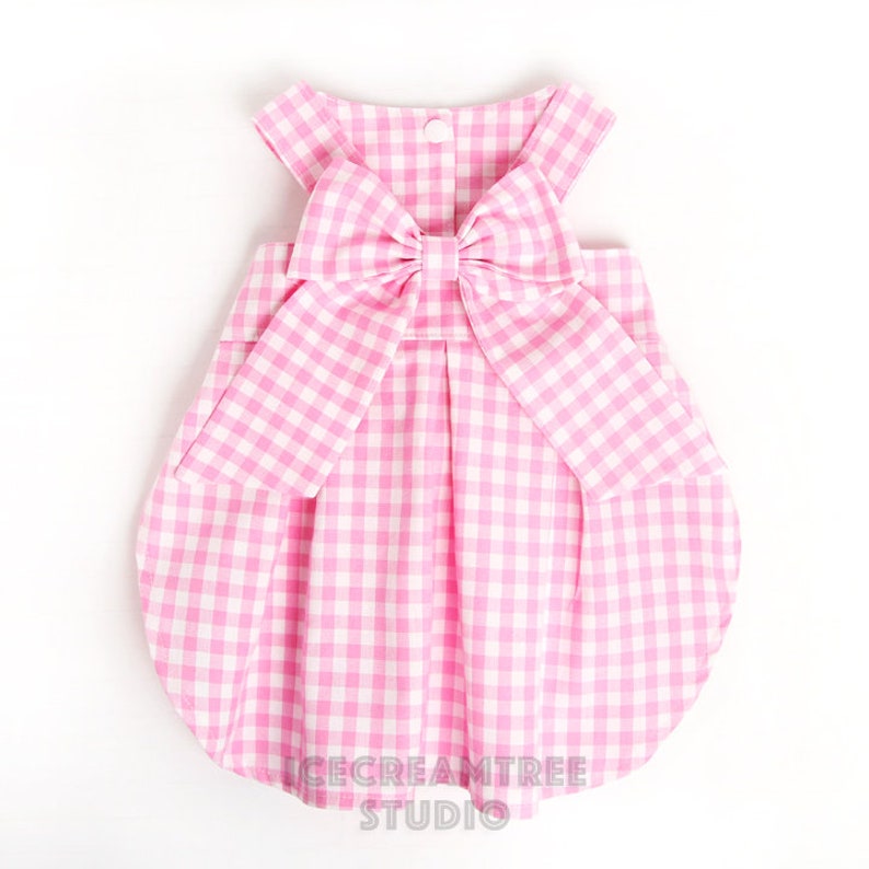 Puede incluir: Vestido de beb&eacute; de vichy rosa y blanco con un gran lazo en la espalda. El vestido tiene una falda fruncida y es sin mangas.
