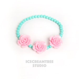 Puede incluir: Un brazalete de cuentas turquesa con tres abalorios de flores rosas.