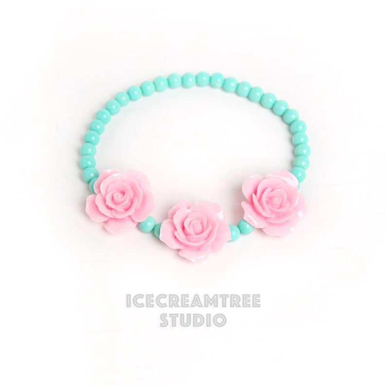 Puede incluir: Un brazalete de cuentas turquesa con tres abalorios de flores rosas.