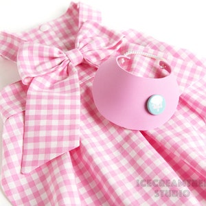 Puede incluir: Vestido de perro de cuadros vichy rosa y blanco con un gran lazo rosa y un collar rosa con un dise&ntilde;o de nube blanca.