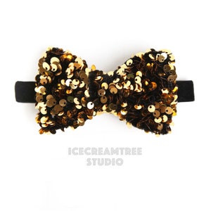 Può includere: Un papillon nero con paillettes dorate. Il papillon è in velluto e ha un elastico nero.