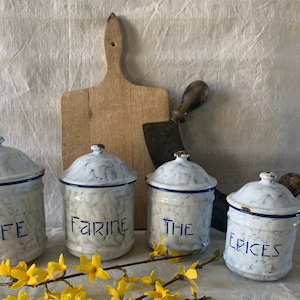 May include: Set of four vintage white ceramic canisters with blue trim and black lettering. The canisters are labelled "Cafe", "Farine", "The", and "Epices".