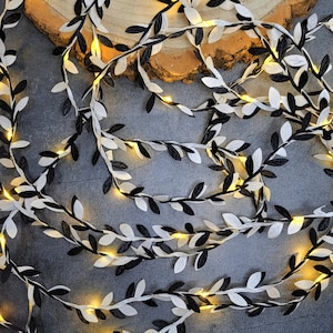 May include: Black and white leaf garland with warm white fairy lights. The garland is made of fabric leaves and is perfect for adding a touch of whimsy to any space.