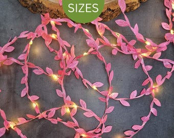 May include: A string of pink artificial vine leaves intertwined with small warm white LED fairy lights. The decorative garland features numerous small pink leaves along a thin wire, with a green circular overlay displaying the text 7 SIZES.