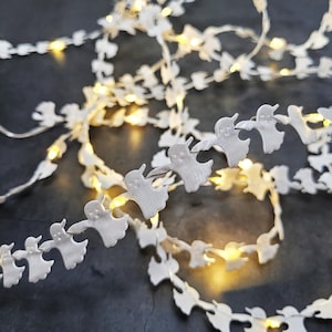 May include: White ghost-shaped LED fairy lights strung together. The lights are warm white and the ghosts are made of a soft, fabric-like material.