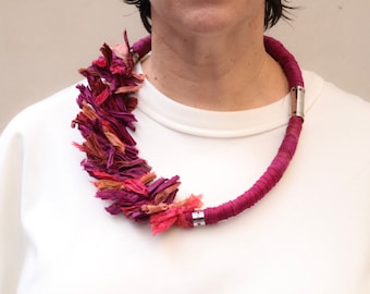 Puede incluir: Un collar de tela rosa y rojo con un cierre plateado. El collar está hecho de muchas pequeñas piezas de tela que están atadas juntas.
